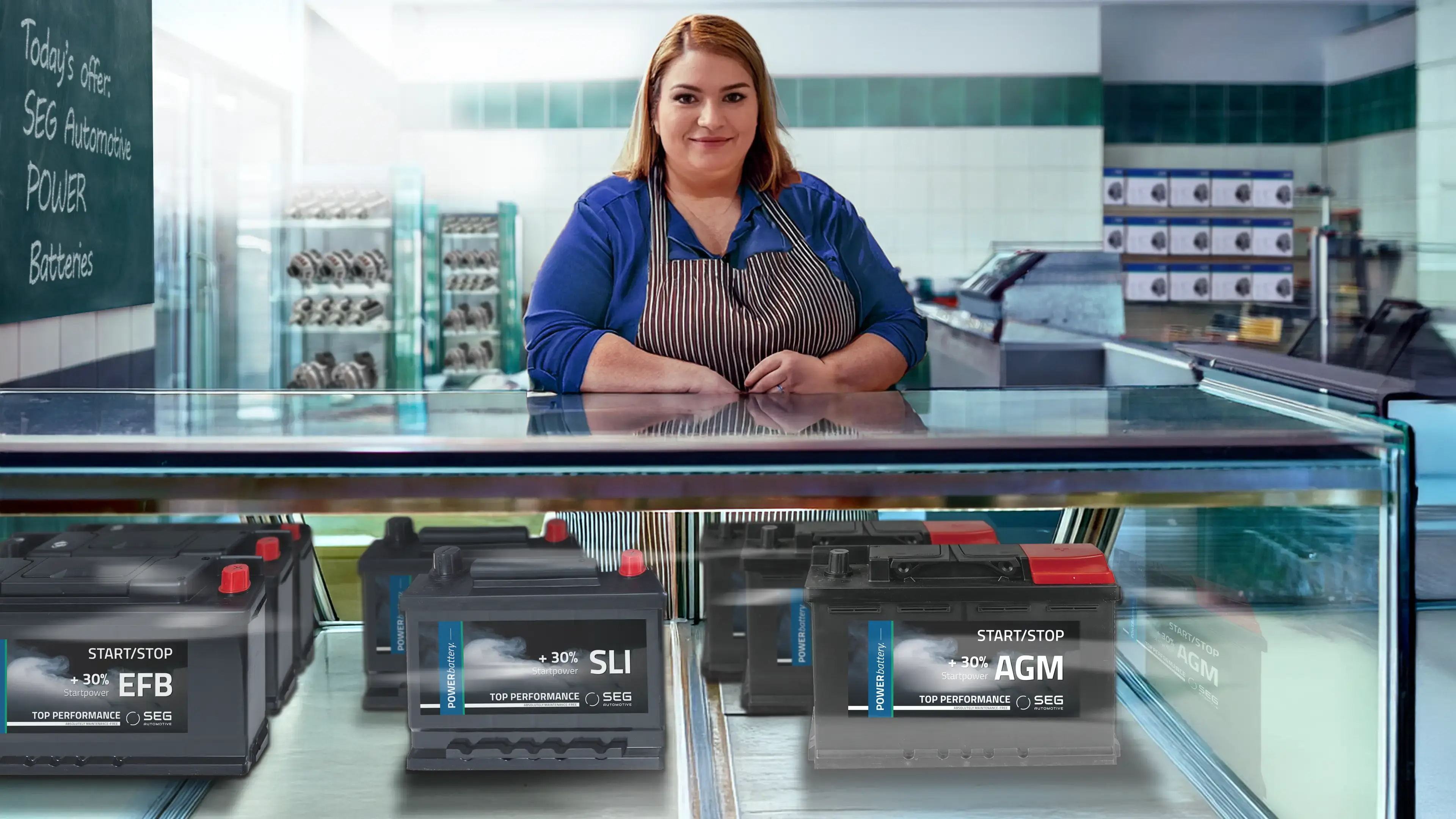 Saleswoman behind a glass counter with car batteries on display.