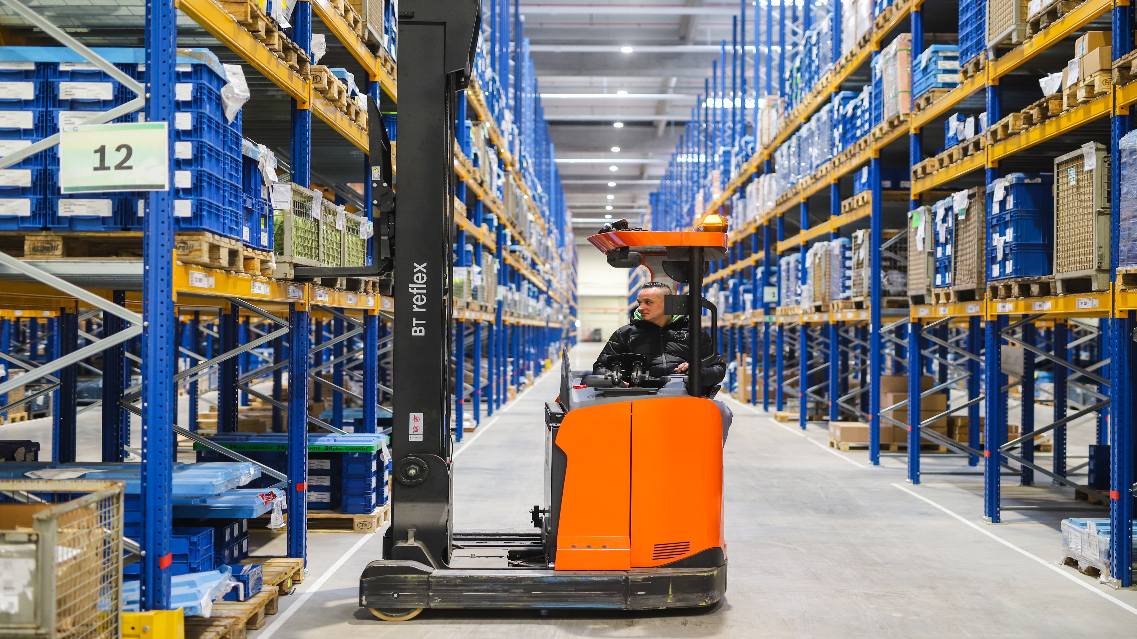 Forklift loads goods into high rack in a logistics center
